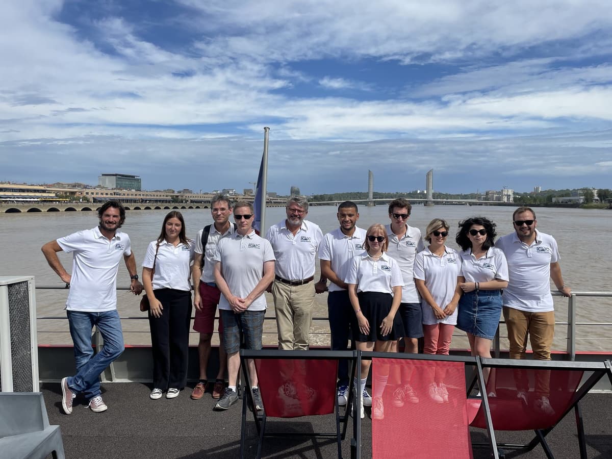 L’équipe du cabinet en polos blancs sur le pont d’un bateau, sur la Garonne, le pont Jacques-Chaban-Delmas au loin